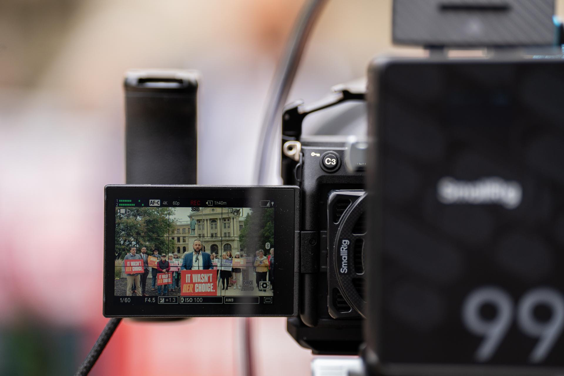 A camera monitor shows Aaron Baer speaking at the press conference