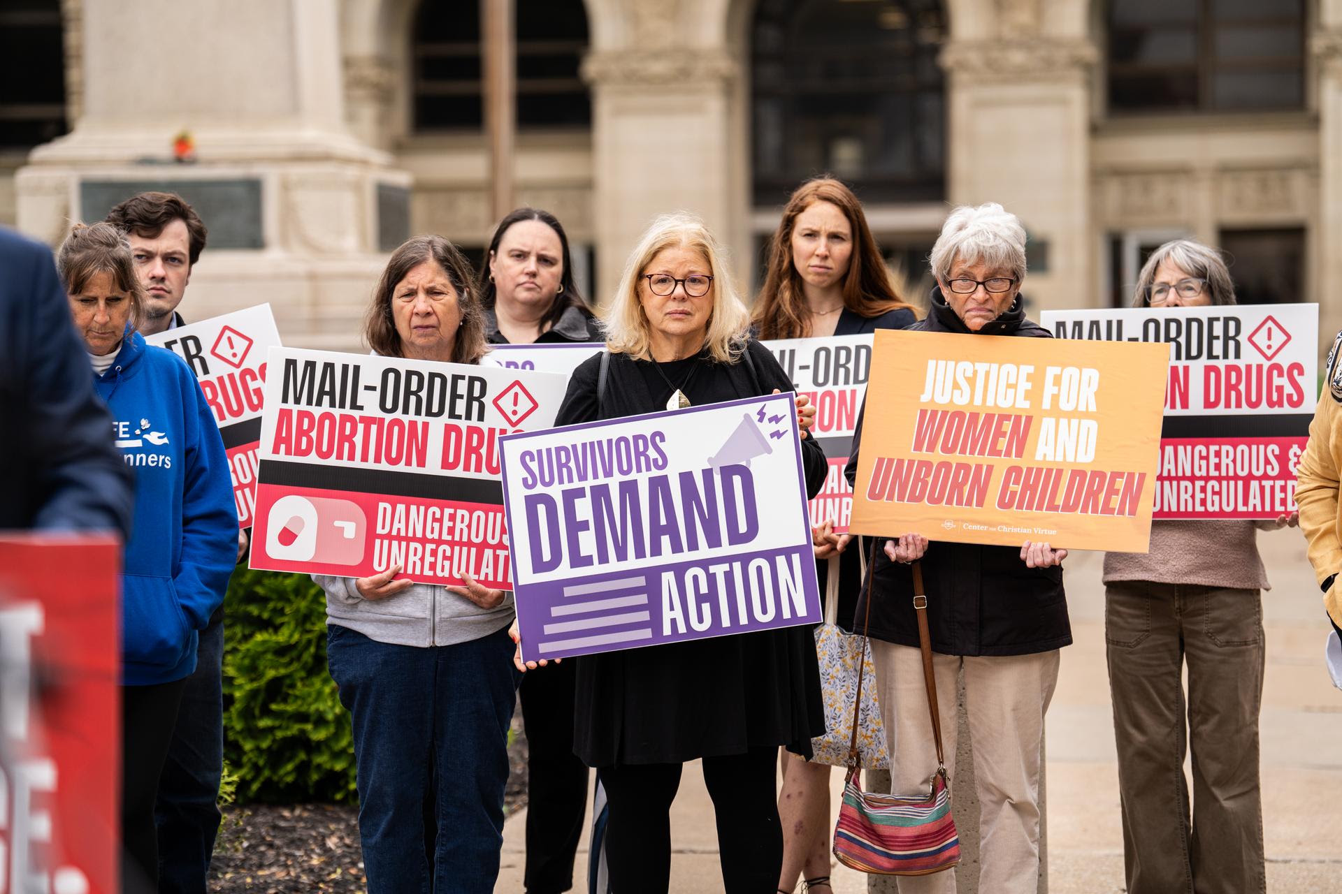 Supporters hold signs reading “Survivors demand action” and “Justice for women and unborn children”