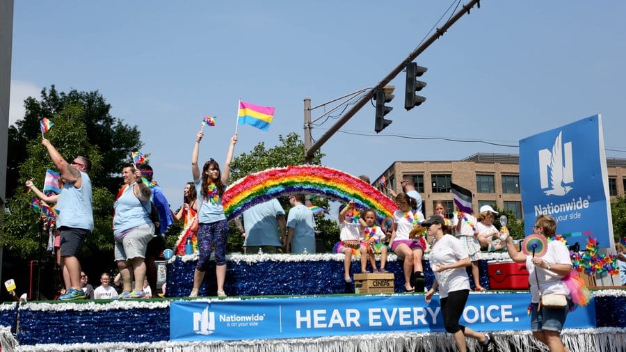 People ride on a decorated float in a pride parade.